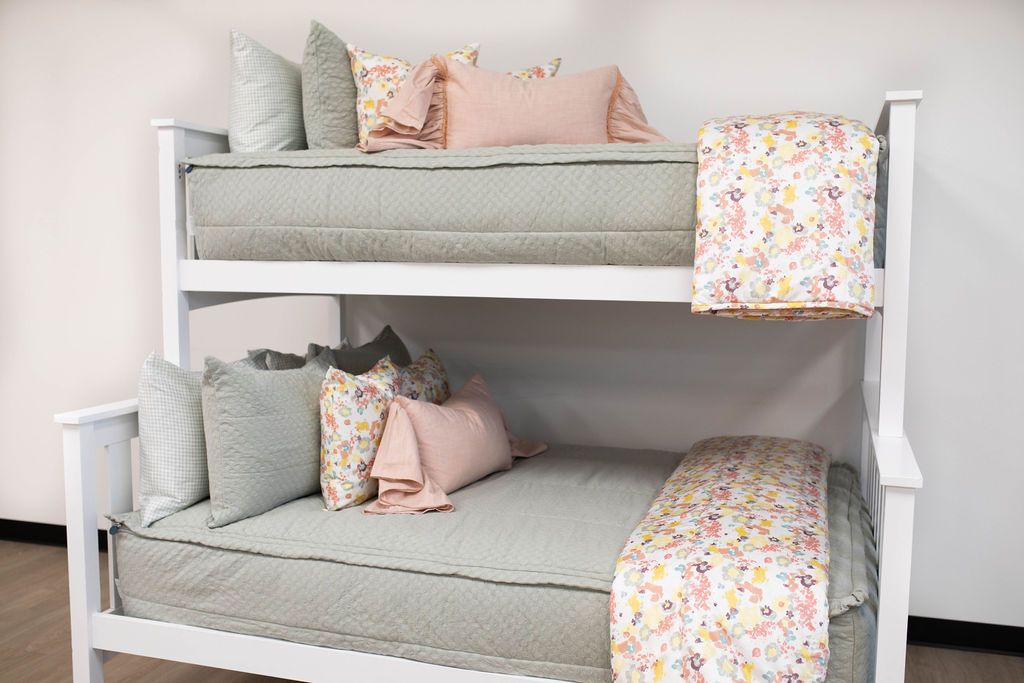 A standard bunk bed with both bunks made with sage green zipper bedding and light pink and multi-colored pillows and blankets.
