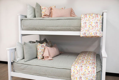 A standard bunk bed with both bunks made with sage green zipper bedding and light pink and multi-colored pillows and blankets.