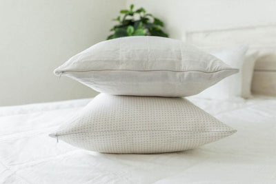 A bed made with white woven plaid zipper bedding and the matching pillows stacked on top of each other in the middle of the bed.
