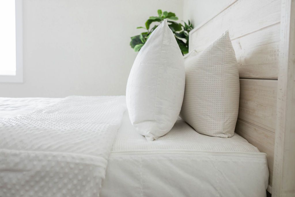 A side view of a bed made with white woven plaid zipper bedding with the top unzipped halfway down the bed and the comforter folded down.