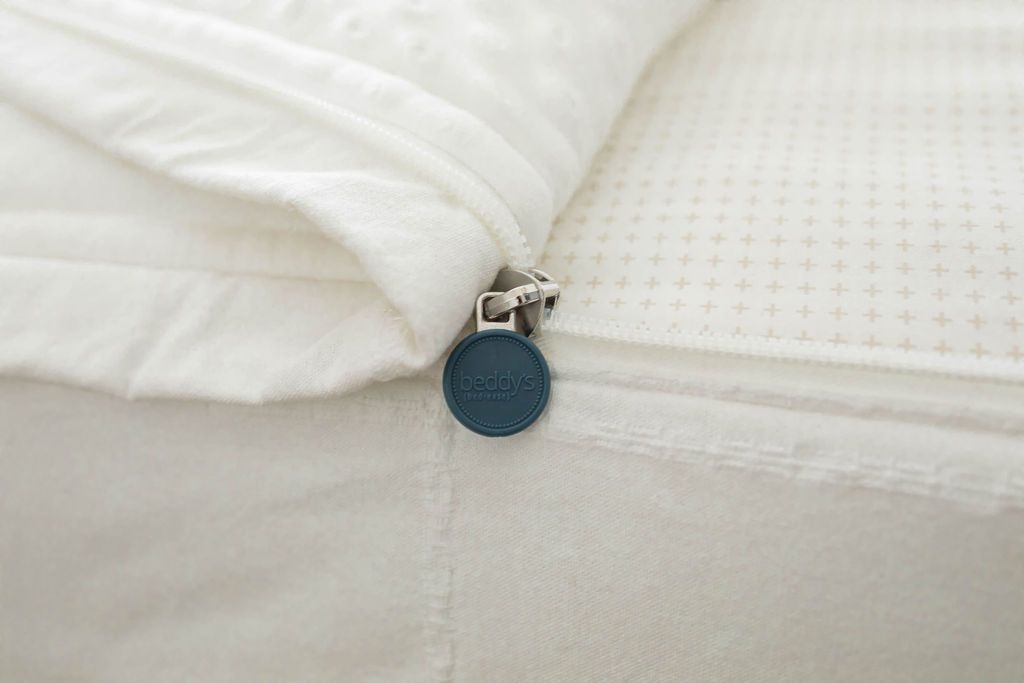 A close up view of a bed made with white woven plaid zipper bedding with the bed slightly unzipped to reveal the minky comforter and the white pattern bottom cotton lining.