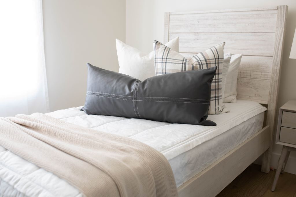 A twin bed made with white woven plaid zipper bedding and an assortment of neutral and striped pillows and matching blanket.