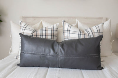 A close up view of a bed made with white woven plaid zipper bedding and an assortment of neutral and leather pillows.