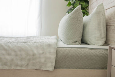 A side view of a bed made with a light green zipper bedding with the top unzipped halfway down and the comforter folded down.