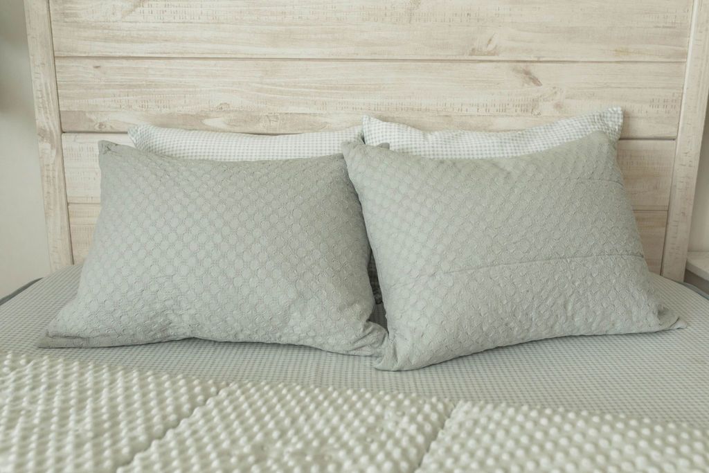A bed made with light green zipper bedding with the comforter pulled back and pillows on top of the bed.