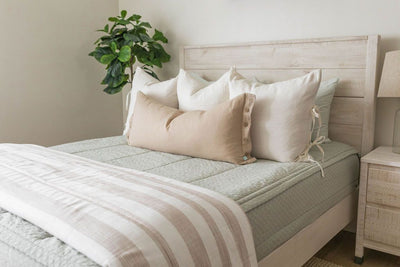 A queen bed made with soft green zipper bedding and neutral white and tan pillows and blanket.