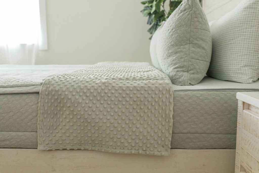 A side view of a bed made with soft green zipper bedding with the top unzipped halfway down the bed and the comforter folded down.