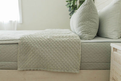 A side view of a bed made with soft green zipper bedding with the top unzipped halfway down the bed and the comforter folded down.