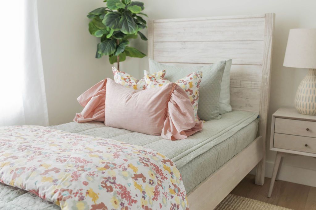 A twin bed made with soft green zipper bedding and pink and multi-color floral pattern pillows and blanket.
