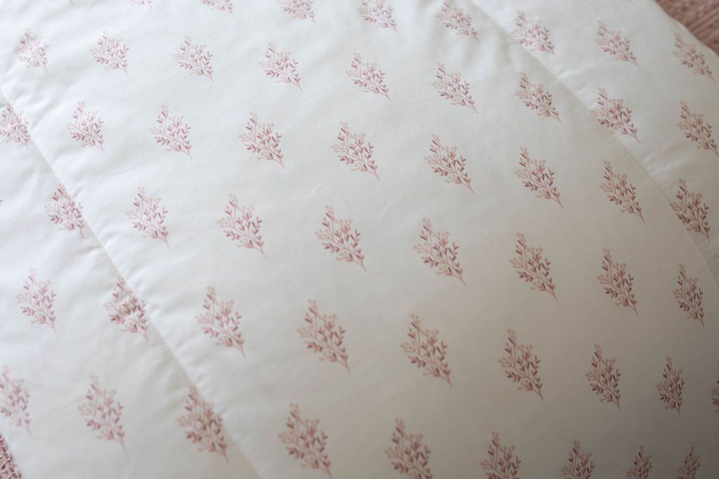 A close up of a white blanket that has a floral pink pattern design. 