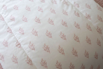 A close up of a white blanket that has a floral pink pattern design. 