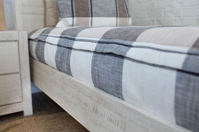 A close up side view of a bed made with cream, tan, and charcoal plaid zipper bedding.