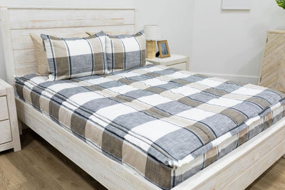 A bed made with cream, charcoal, and tan plaid zipper bedding and matching pillows.
