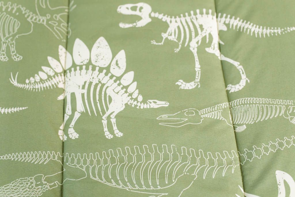 A close up of the print on a set of olive green dinosaur fossils kids zipper bedding.