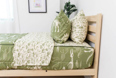 A side shot of a twin bed made with olive green dinosaur fossils kids zipper bedding, the top unzipped and pulled back slightly and two pillows at the head of the bed.
