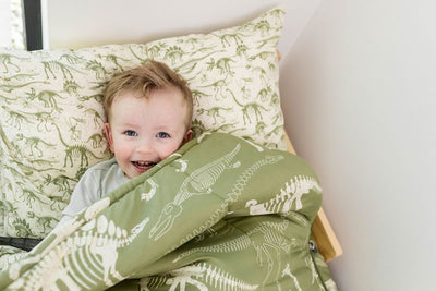 A young boy awake in a bed made with  olive green dinosaur fossils kids zipper bedding.