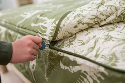 A young child pulling the zipper closed on a set of olive green dinosaur fossils kids zipper bedding.