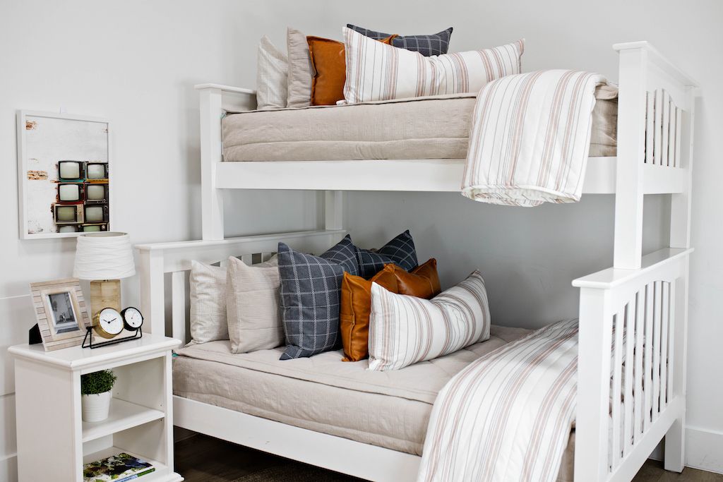 A standard bunk bed with both bunks made with light tan zipper bedding and neutral and leather pillows and blankets.