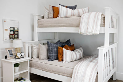 A standard bunk bed with both bunks made with light tan zipper bedding and neutral and leather pillows and blankets.