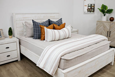 A queen bed made with light tan zipper bedding and neutral pattern pillows and blanket.