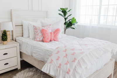 White twin bedframe with white textured bedding, pink and white striped euro with ruffle, white and pink butterfly print pillow, pink plush butterfly pillow, and white and pink print blanket with white ruffle along the edge