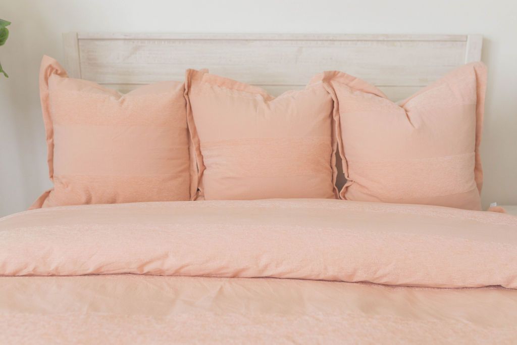 A bed made with a peach zipper duvet folded and matching large pillows.