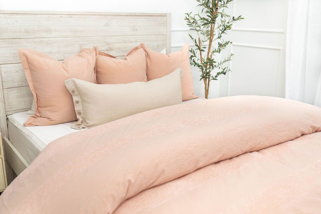 A brightly lit bedroom with a bed made with white zipper sheets and a peach zipper duvet folded half way down the bed and adorned with matching peach and neutral pillows.