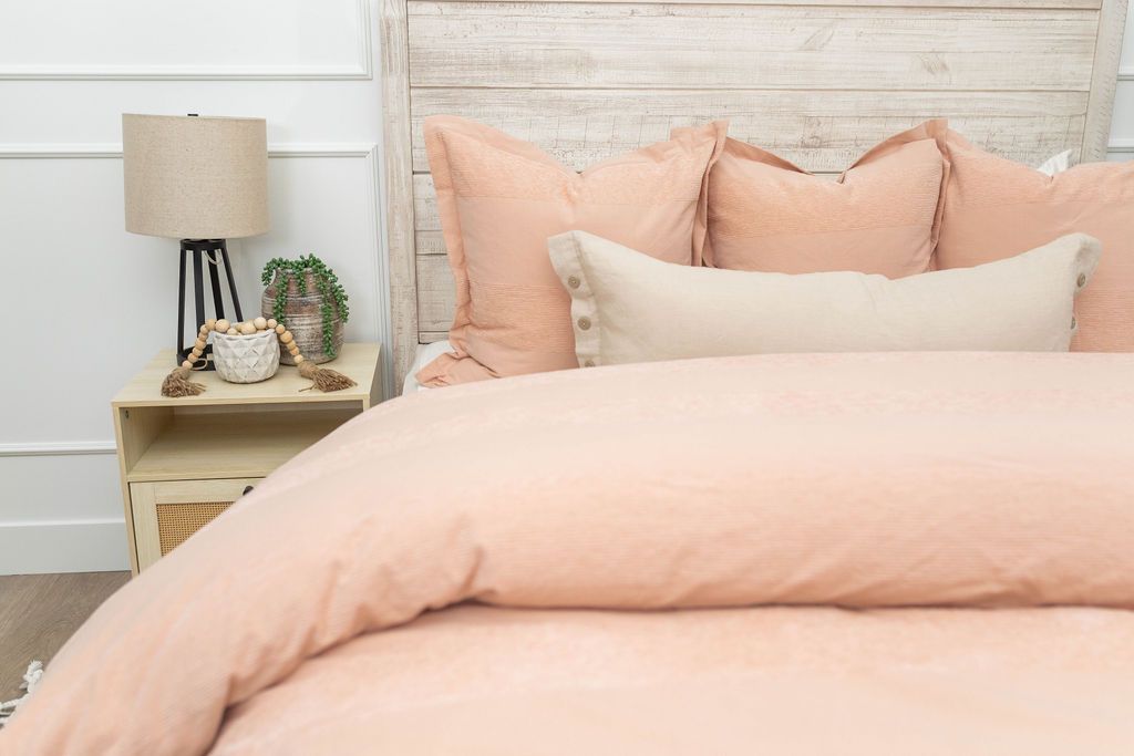 A bed made with a peach zipper duvet folded half way down the bed and adorned with matching peach and neutral pillows.