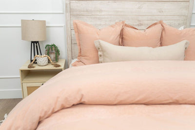 A bed made with a peach zipper duvet folded half way down the bed and adorned with matching peach and neutral pillows.