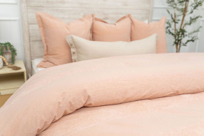 A close up view of a bed made with white zipper sheets and a peach zipper duvet folded half way down the bed and adorned with matching peach and neutral pillows.
