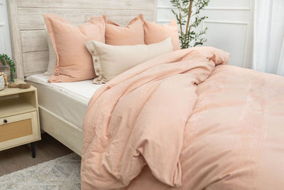 A brightly lit bedroom with a bed made with white zipper sheets and a peach zipper duvet folded partially half way down the bed and adorned with matching peach and neutral pillows.