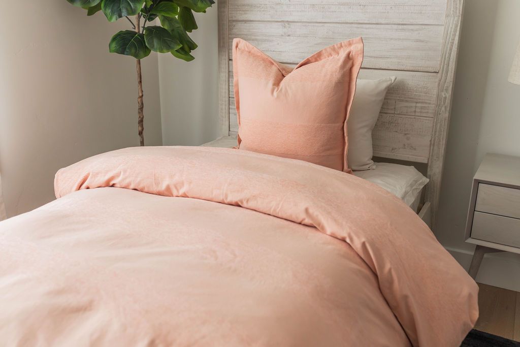 A twin bed made with white zipper sheets and a peach zipper duvet folded half way down the bed and adorned with a peach pillow.