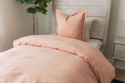 A twin bed made with white zipper sheets and a peach zipper duvet folded half way down the bed and adorned with a peach pillow.