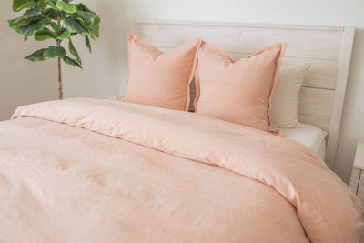 A bed made with white zipper sheets and a peach zipper duvet partially folded down the bed and adorned with matching large pillows.