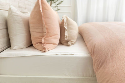 A side view of a bed made with white zipper sheets and a peach zipper duvet folded half way down the bed and adorned with neutral and matching pillows.