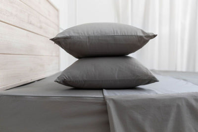 A side view of a bed made with gray zipper sheets and the top sheet slightly unzipped and folded with the matching pillows stacked on top of each other.