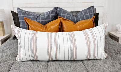 A close up view of a bed made with deep gray and brown zipper bedding and adorned with neutral gray, leather, and striped pillows.