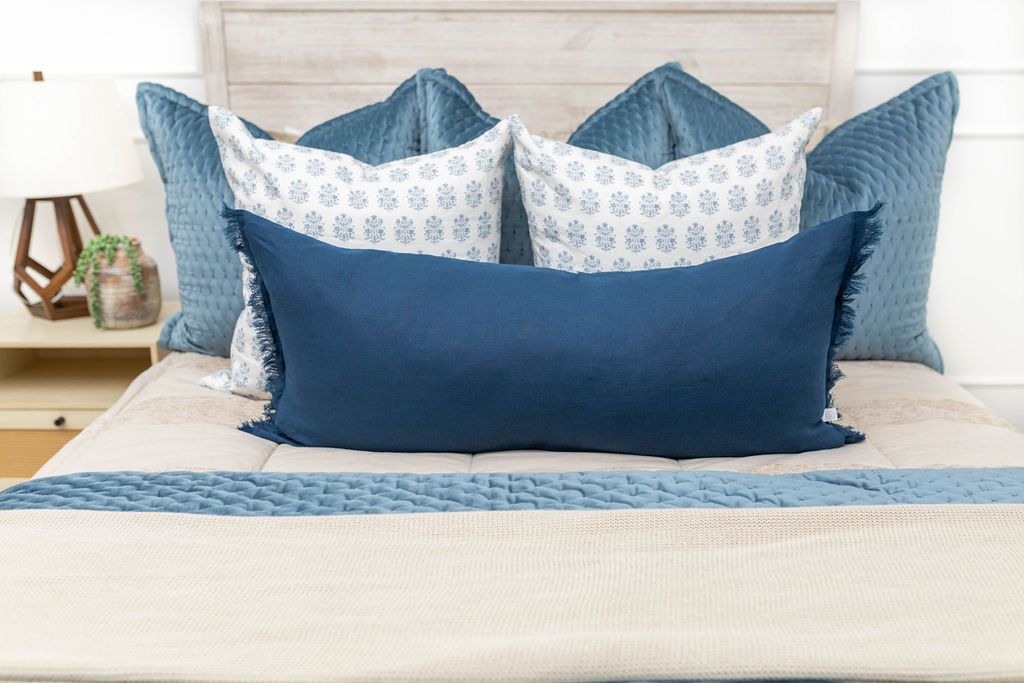 A close up view of a bed made with tan faded stripes zipper bedding and an assortment of neutral and blue velvet pattern throw pillows and matching blankets.