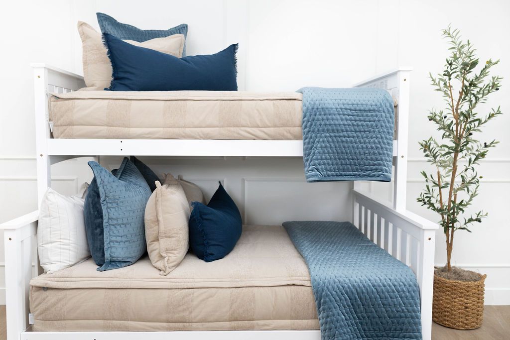 A standard bunk bed with both bunks made with tan faded stripes zipper bedding and neutral and blue velvet pillows and blankets.