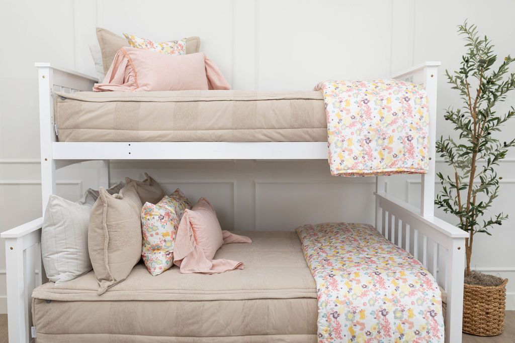 A standard bunk bed with both bunks made with tan faded stripes zipper bedding and neutral and multicolored floral pink pillows and blankets.