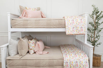 A standard bunk bed with both bunks made with tan faded stripes zipper bedding and neutral and multicolored floral pink pillows and blankets.