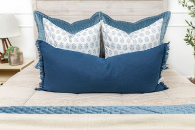 A close up view of a bed made with tan faded stripes zipper bedding and an assortment of neutral and blue velvet pattern throw pillows and matching blankets.