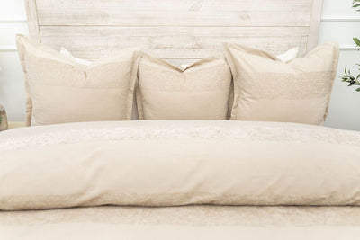 A bed made with a tan zipper duvet folded partially down the bed and adorned with neutral matching pillows.