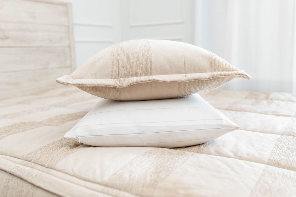 A white and tan striped pillowcase and matching sham on a made bed with tan striped zipper bedding. 