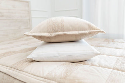 A white and tan striped pillowcase and matching sham on a made bed with tan striped zipper bedding. 