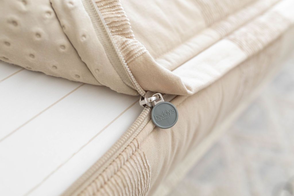 A close up view of a bed made with tan faded stripes zipper bedding with the bed slightly unzipped to reveal the minky comforter and the tan and white striped bottom cotton lining.