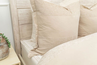 A close up view of a bed made with white zipper sheets and a tan zipper duvet folded partially down the bed and adorned with neutral large matching tan pillows.