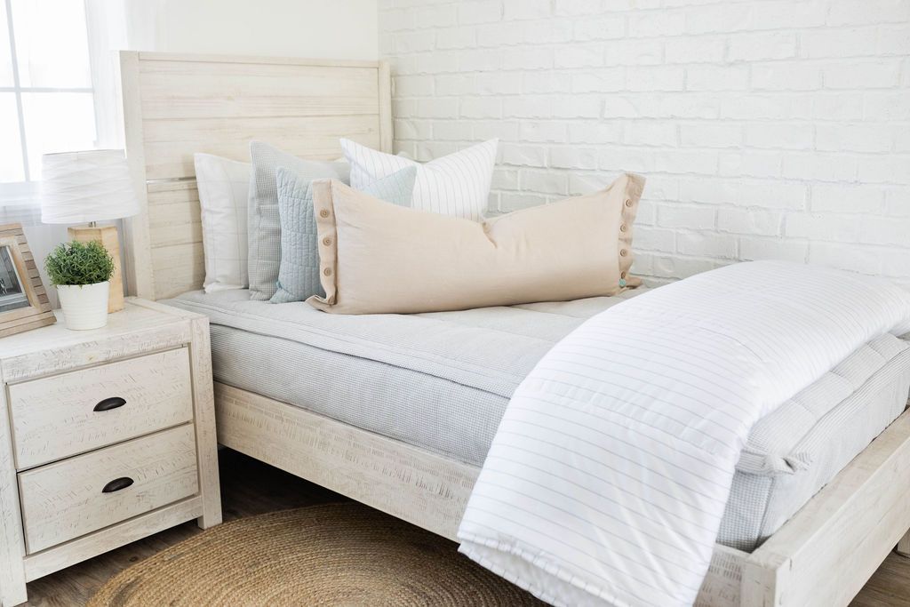 A twin bed made with light gray waffle textured zipper bedding and an assortment of neutral and light blue pillows and blanket.