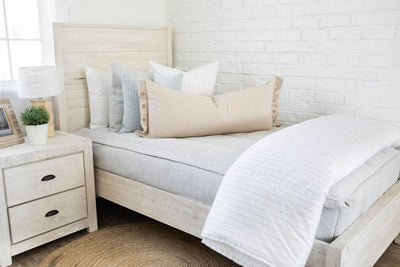 A twin bed made with light gray waffle textured zipper bedding and an assortment of neutral and light blue pillows and blanket.