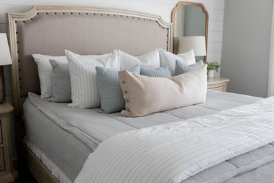 A bed made with light gray waffle texture zipper bedding and an assortment of neutral and striped pillows and matching blanket.